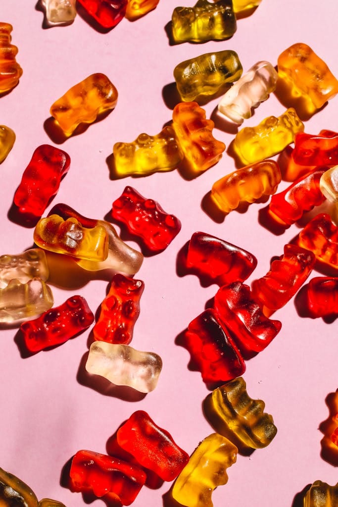 Close-up of assorted gummy bears on a pastel pink surface.